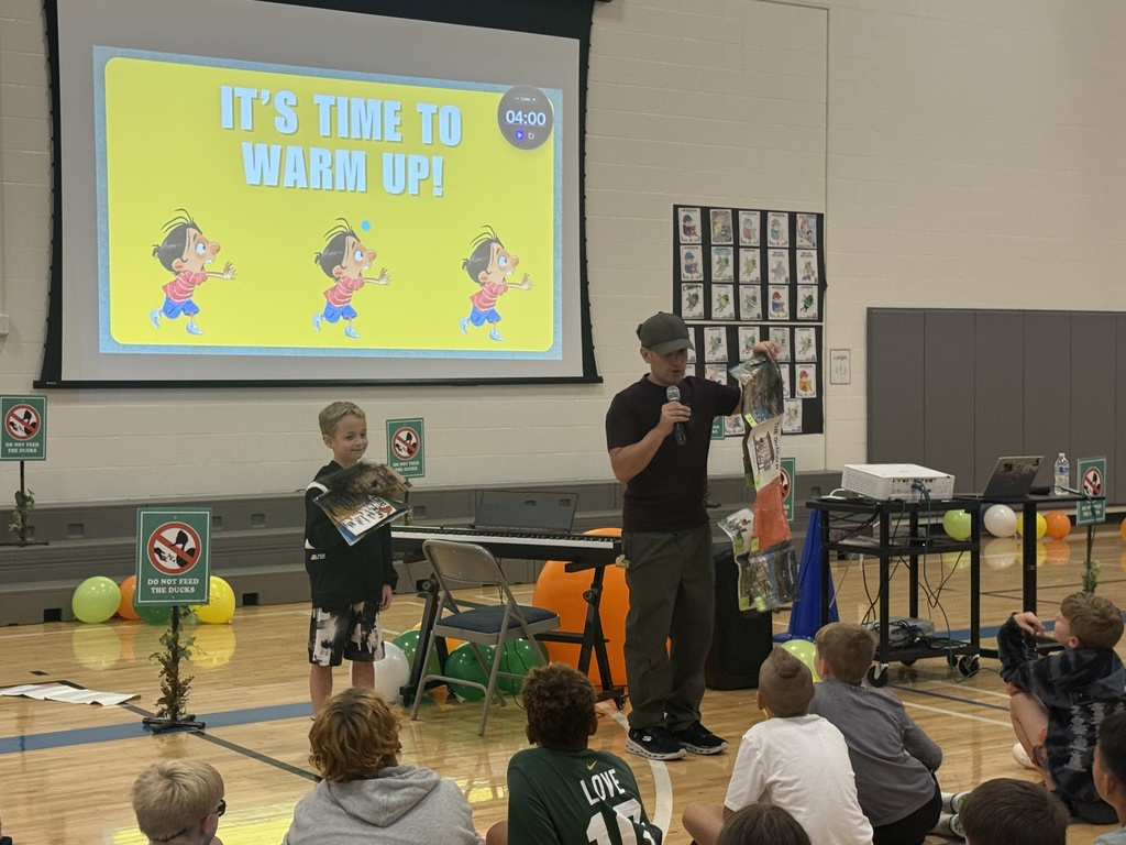 Justin stands next to a male fourth grade student.  The student holds the book jacket while Justin models the inside pages at the start of the printing process in a long sheet.