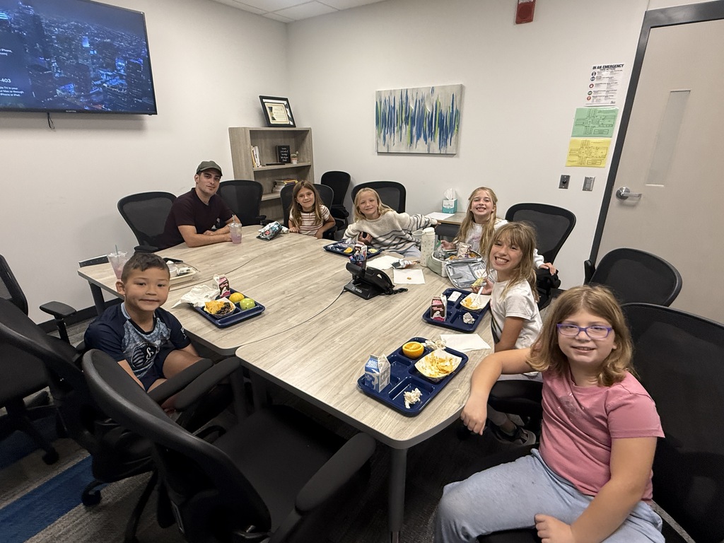 Five third grade girls and one third grade boy sit with Justin eating lunch.