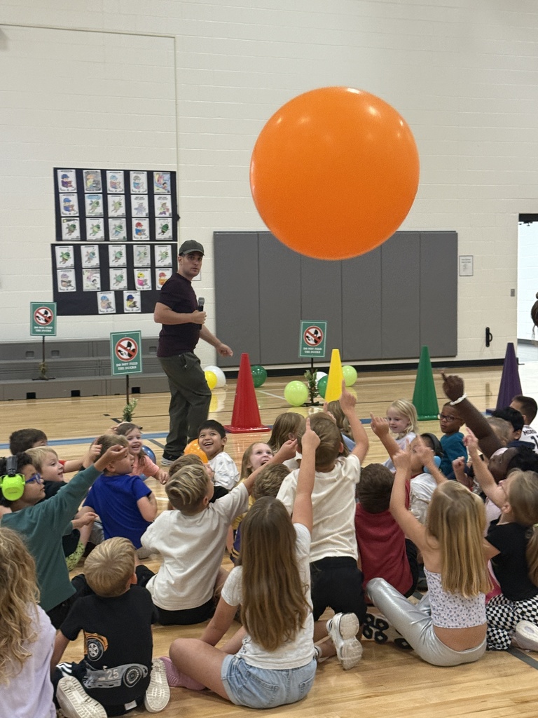Students sit on the floor reaching for an oversized orange balloon that Justin has tossed at them.