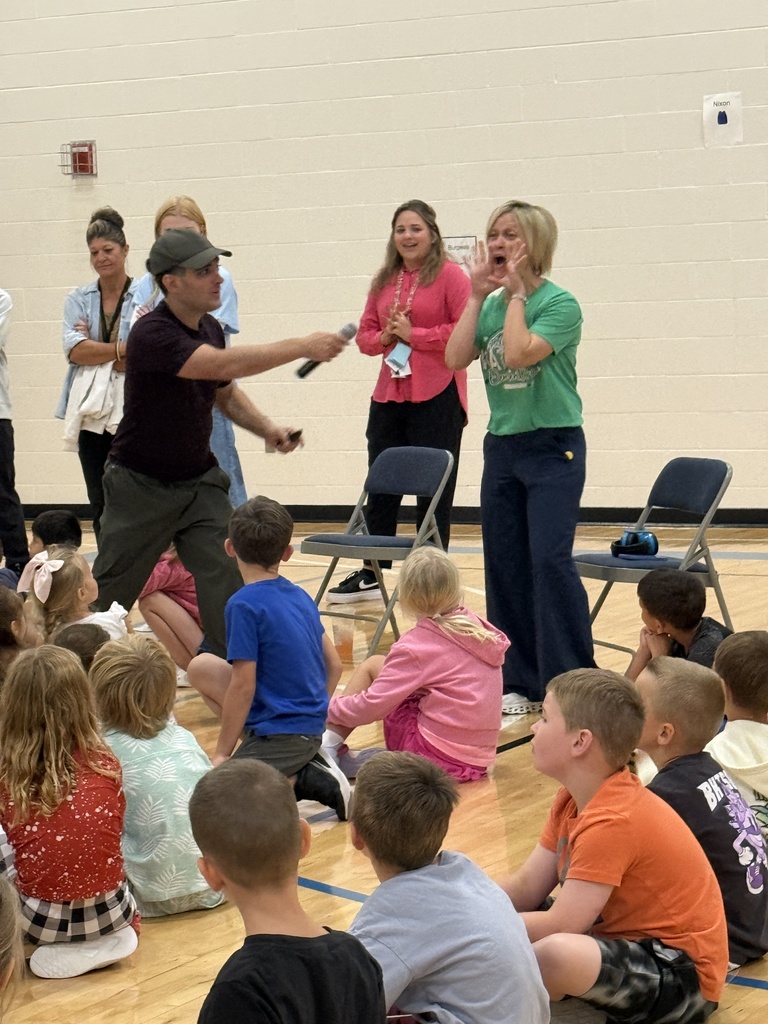 Justin holds the microphone in front of Mrs. Conway.  She has her hands on either side of her mouth to quack.