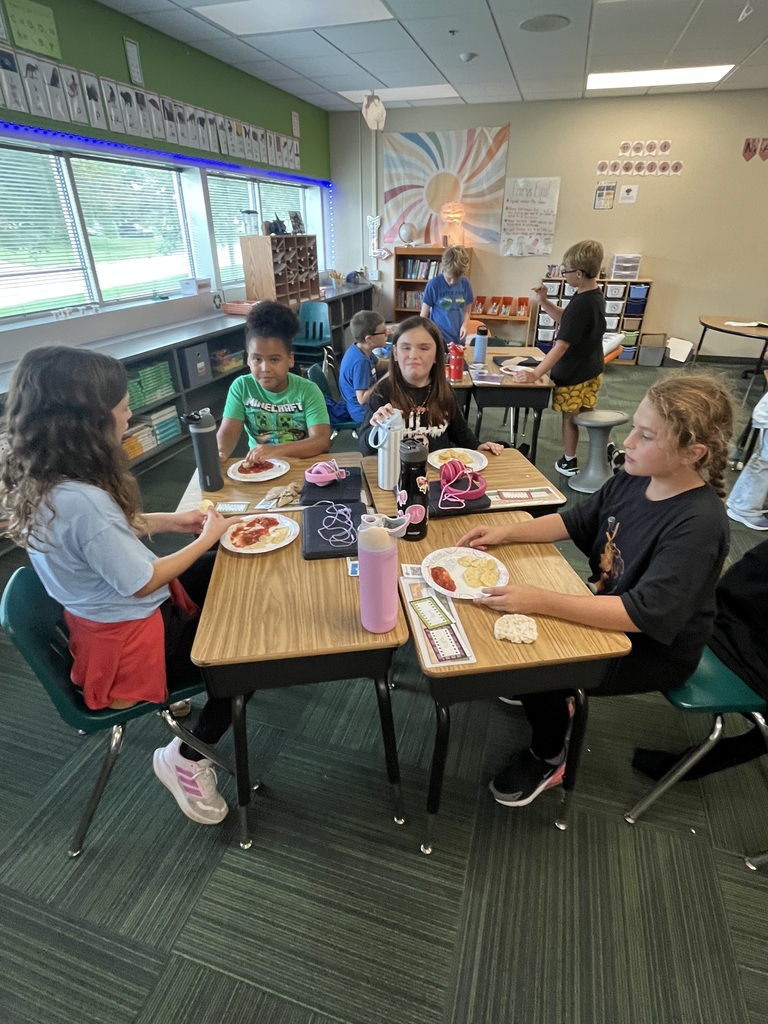 Students seated around a cluster of desks enjoying snacks together in the classroom.