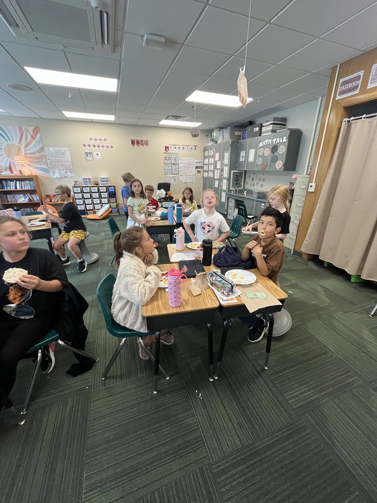 Students spread throughout the classroom sitting at their desks while enjoying snacks.