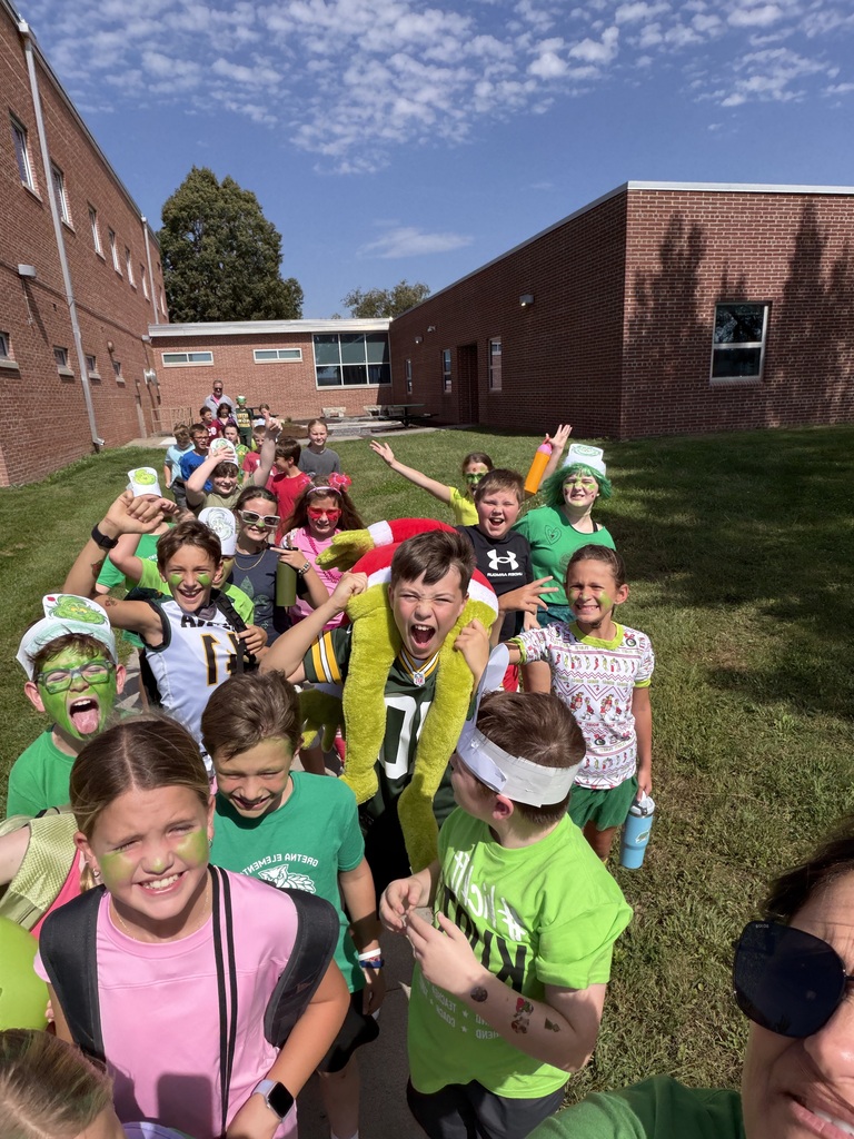 A group of energetic students walking outside together while one carries a plush Grinch figure on his shoulders.