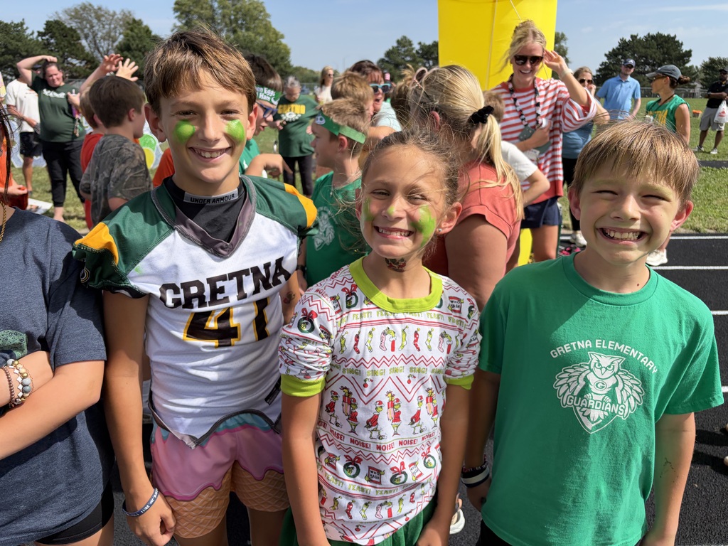 Three elementary students with green face paint smiling together on the running track during a outdoor event.