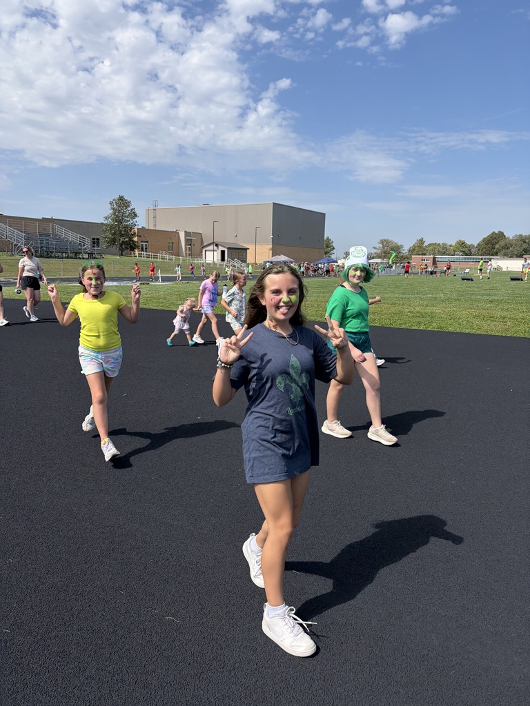 Girls throwing peace signs while walking on the outdoor track during a school activity.