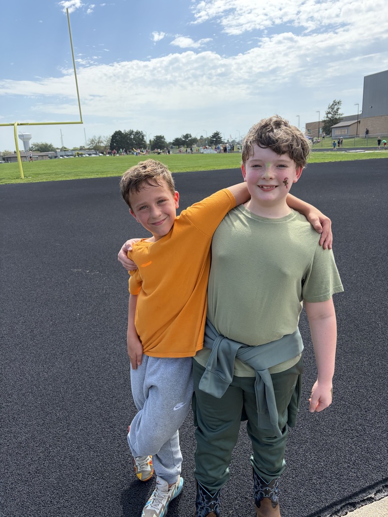 Two boys posing together with arms around each other on a running track next to a football field.