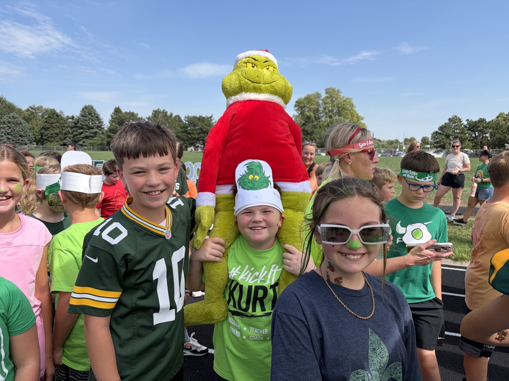 Students posing outdoors while one holds a large plush Grinch mascot above their heads.