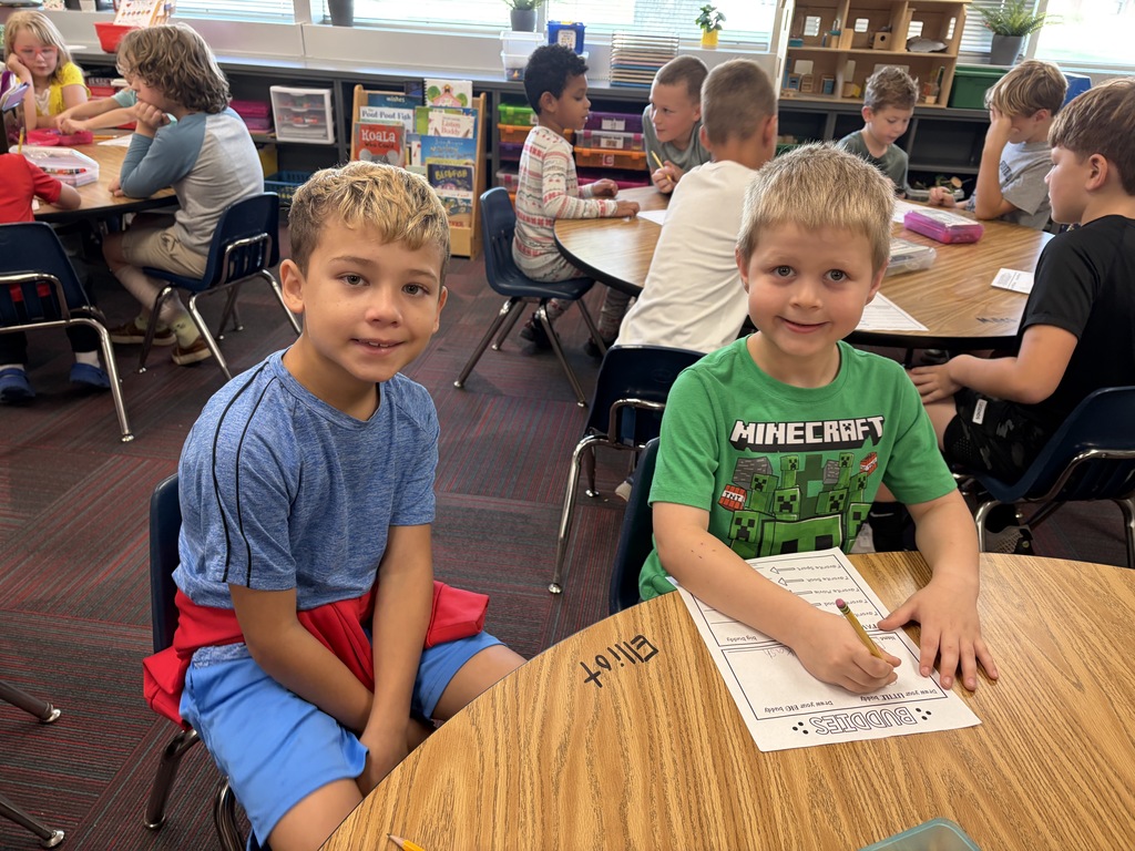 Two young boys sitting together at a wooden table smiling, with one wearing a green Minecraft shirt.