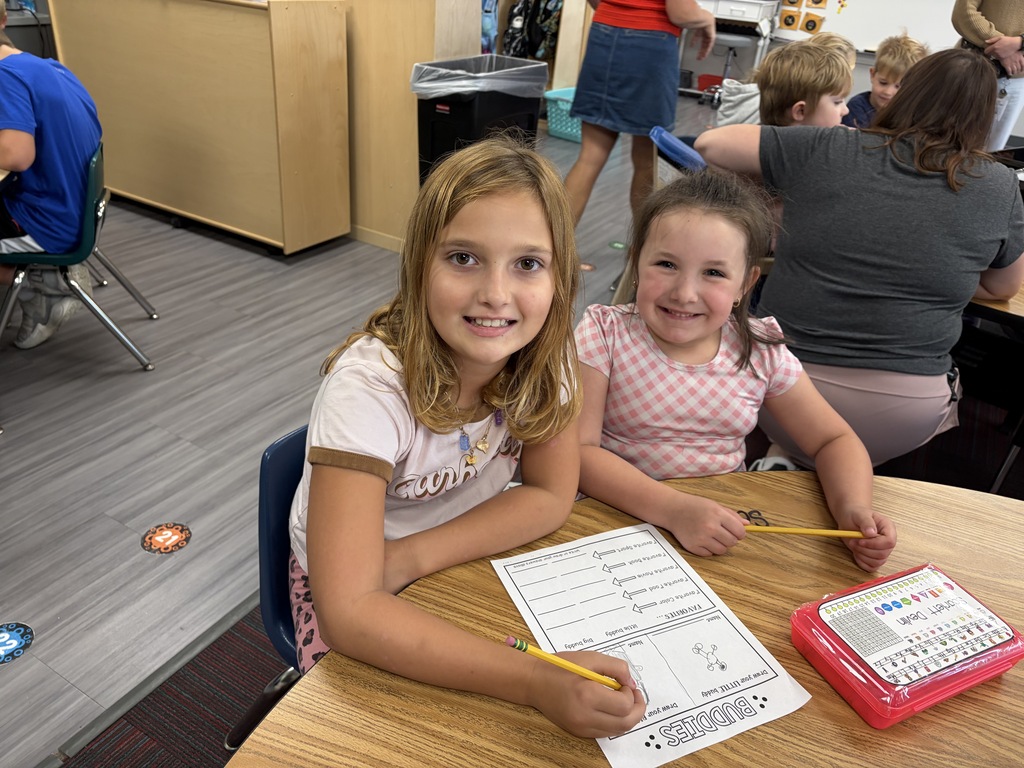 Two young girls sitting next to each other at a desk with pencils and worksheets in a classroom.