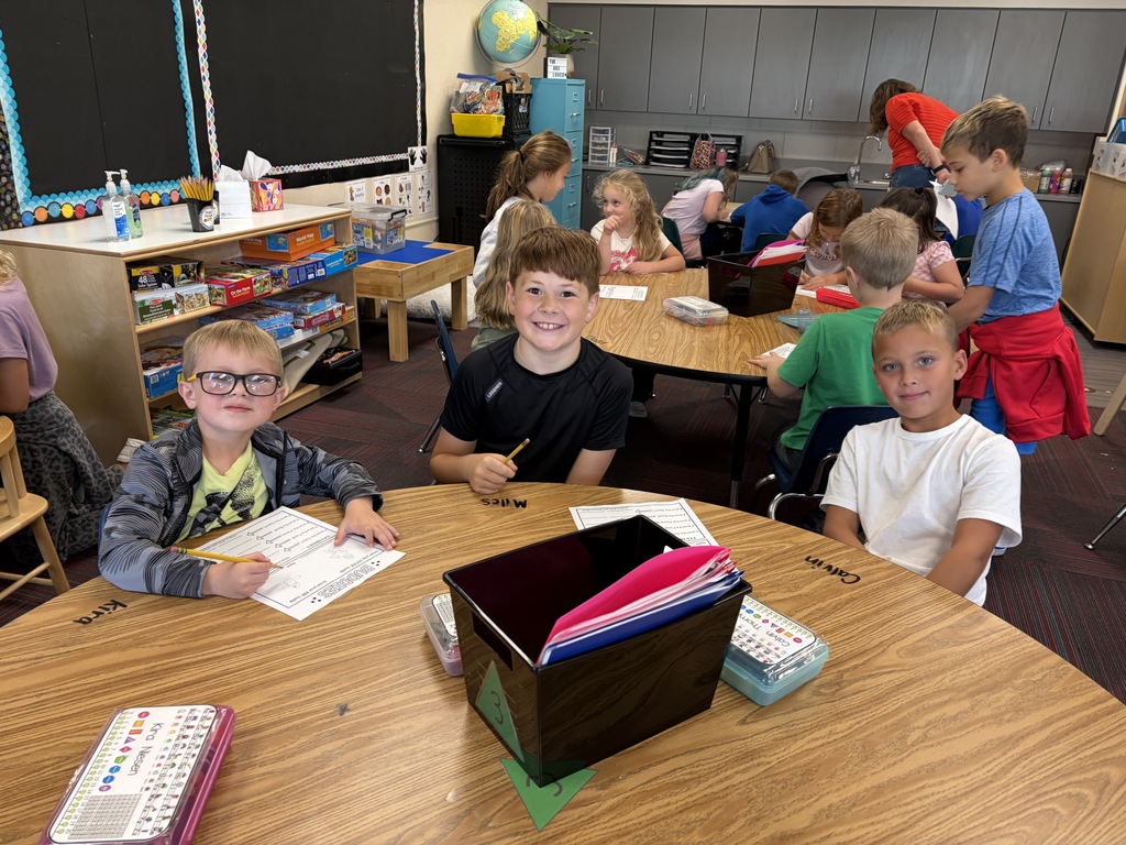 Three young boys sitting together at a round table in a active classroom environment.