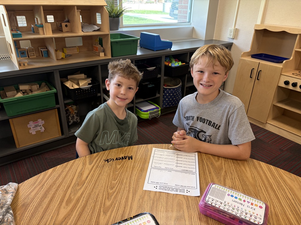 Three young boys sitting together at a round table in a active classroom environment.