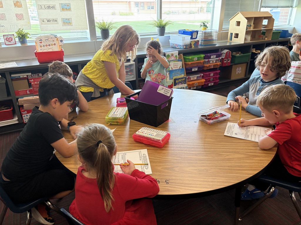 A group of students gathering around a large round table in a classroom doing a table activity.