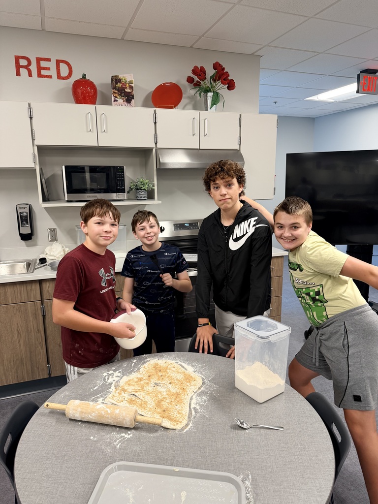 A group of male students stand by a table and smile at the camera. 
