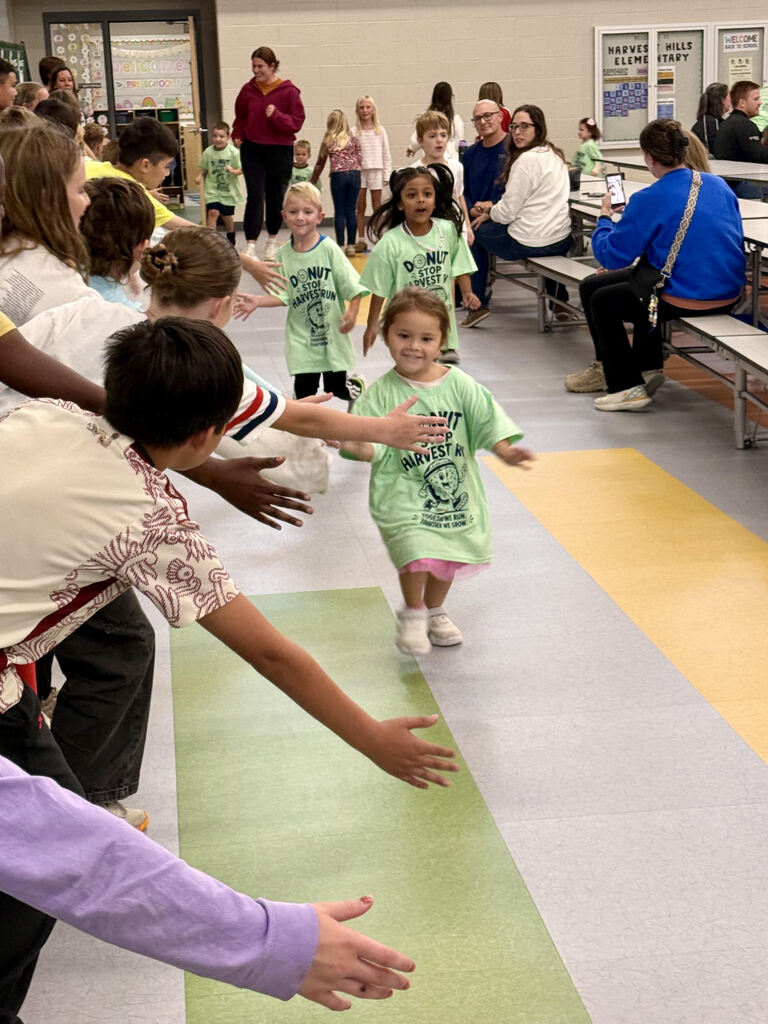 student running at the harvest run taking high fives from older students watching