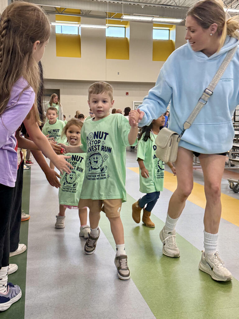 student runing at the harvest run while an older student extends their hand for a high five