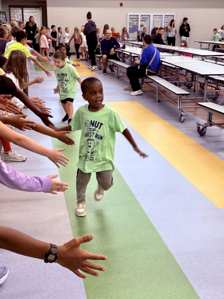 student running at the harvest run taking high fives from older students watching