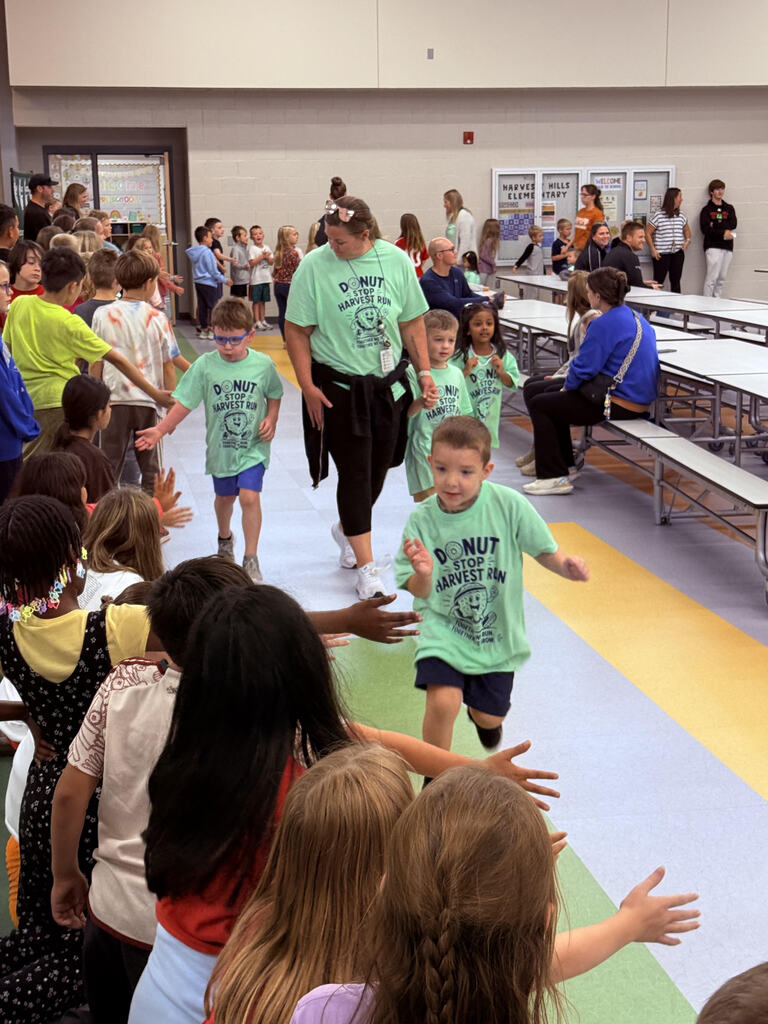preschool students running at the harvest run taking high fives from older students watching