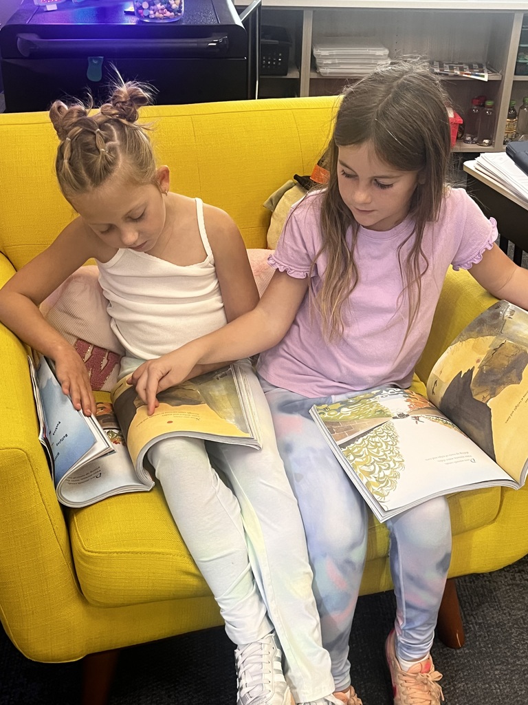 two girls sharing a chair reading a story together
