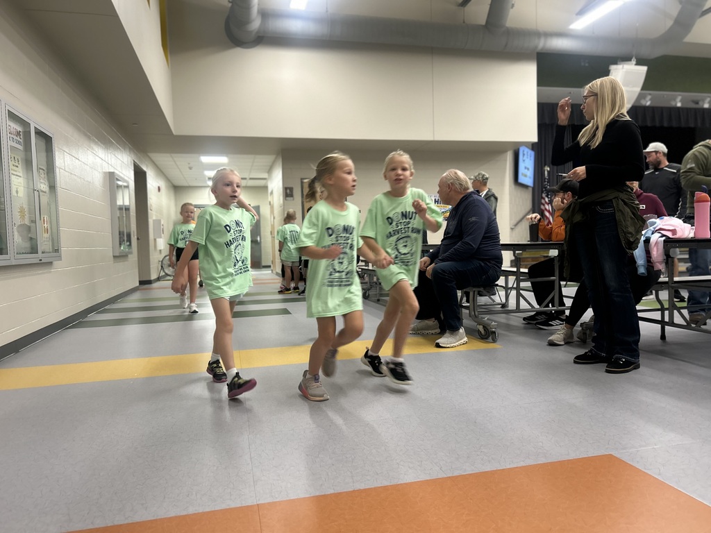 students running in the cafeteria for a fun run at Harvest hills elemtentary. three girls run side by side