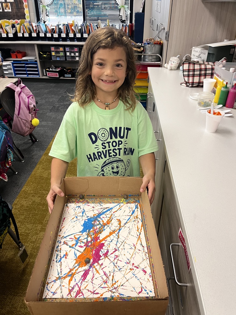 student smilies at the camera working on a painting project in class with marbles on a white paper
