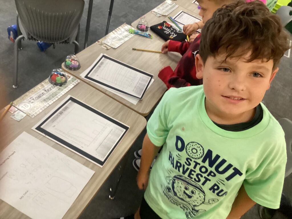 student working on a data sheet at their desk smiling at the camera