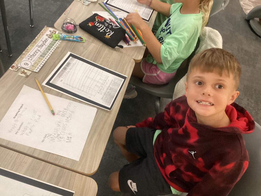 student working on a data sheet at their desk smiling at the camera