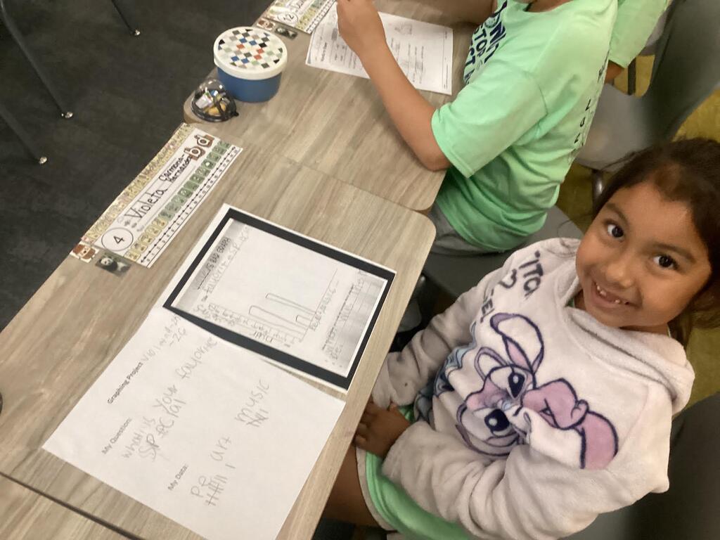student working on a data sheet at their desk smiling at the camera