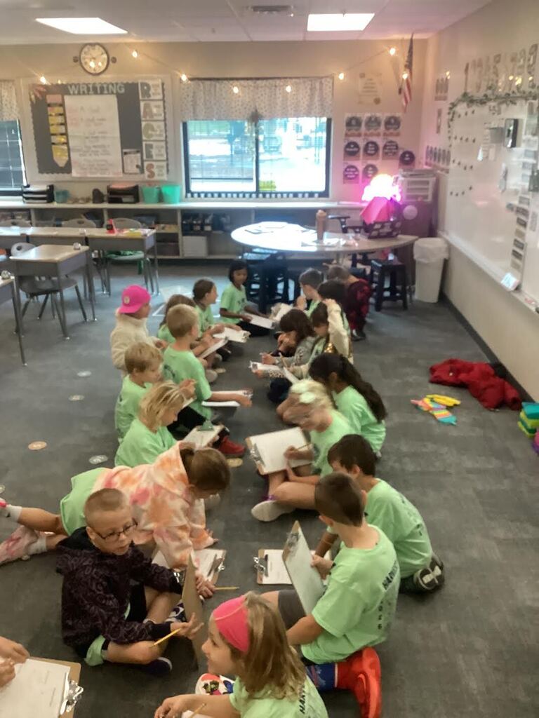 several student seated on the floor working on data using a sheet of paper and a clipboard