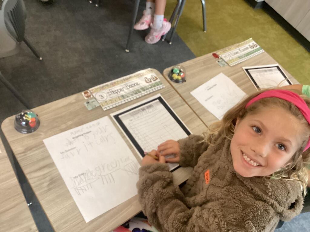 student working on a data sheet at their desk smiling at the camera