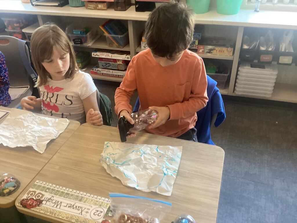 students spraying water on paper for a science project. Student is standing at their desk.