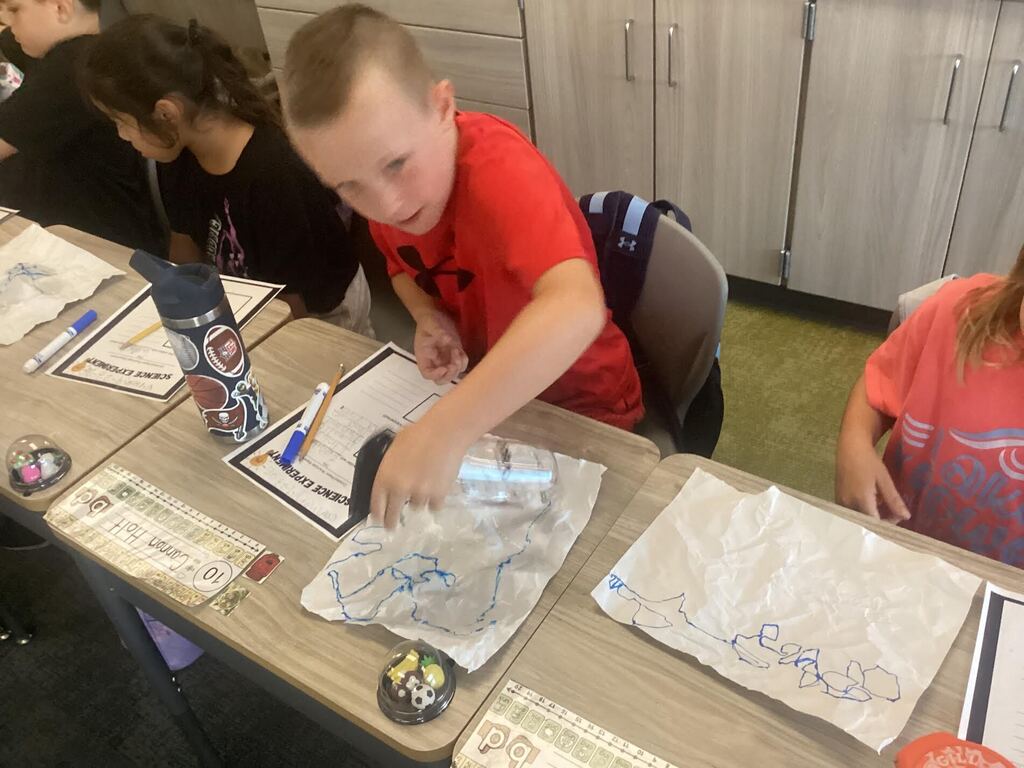 students spraying water on paper for a science project. They are seated at their desk.