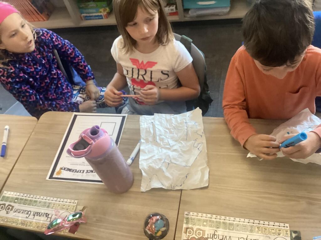 student watching another peer spray water on their paper for a science project.
