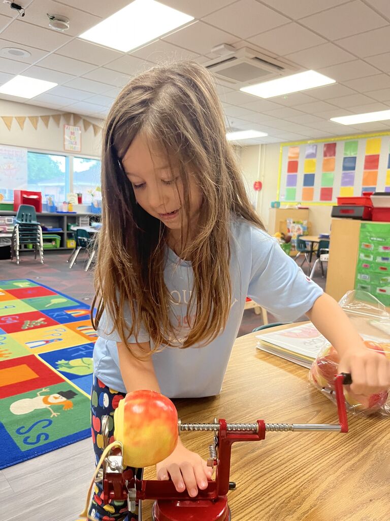 A young girl concentrating as she cranks a red hand-crank apple peeler attached to a wooden table.