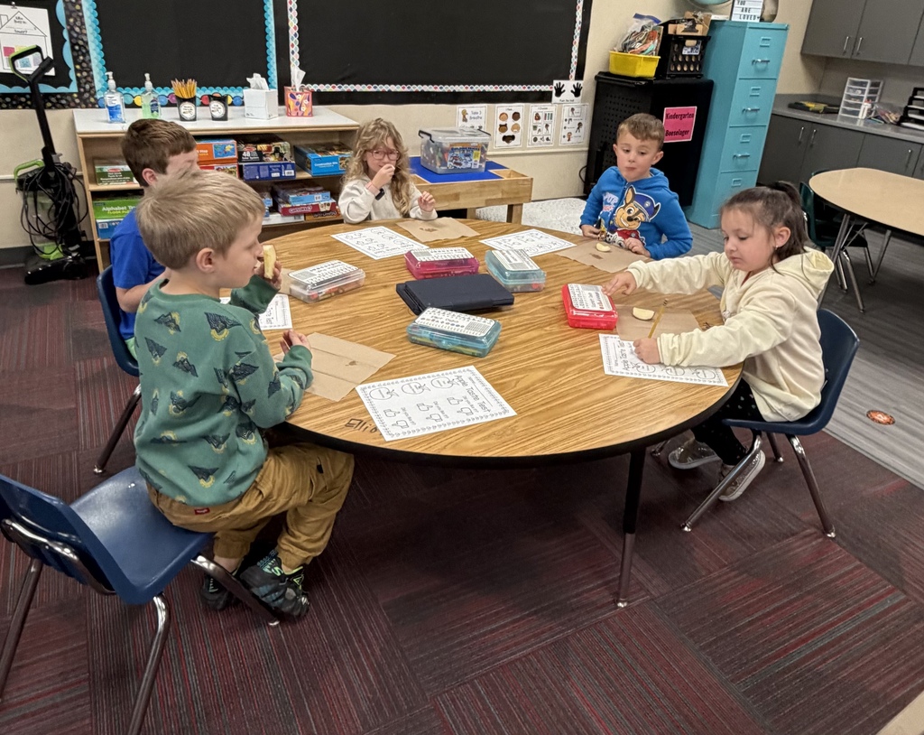 A group of kindergarten students seated at a round table trying different apple slices and recording their results.