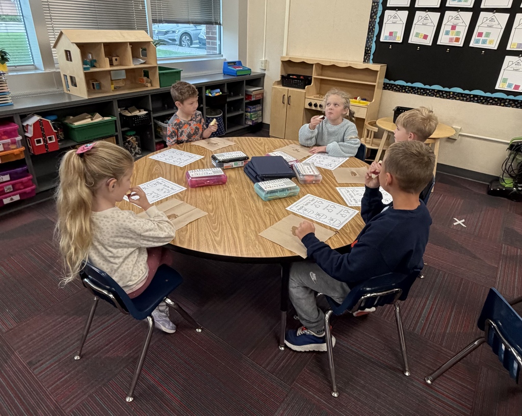 Students gathered around a circular table in a classroom during an apple taste testing activity.