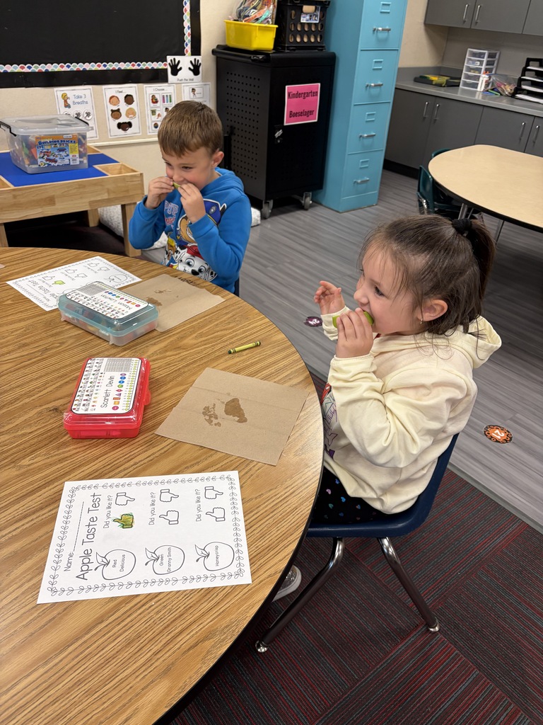 Two young students enjoying green apple slices at a classroom round table next to their "Apple Taste Test" activity sheets.