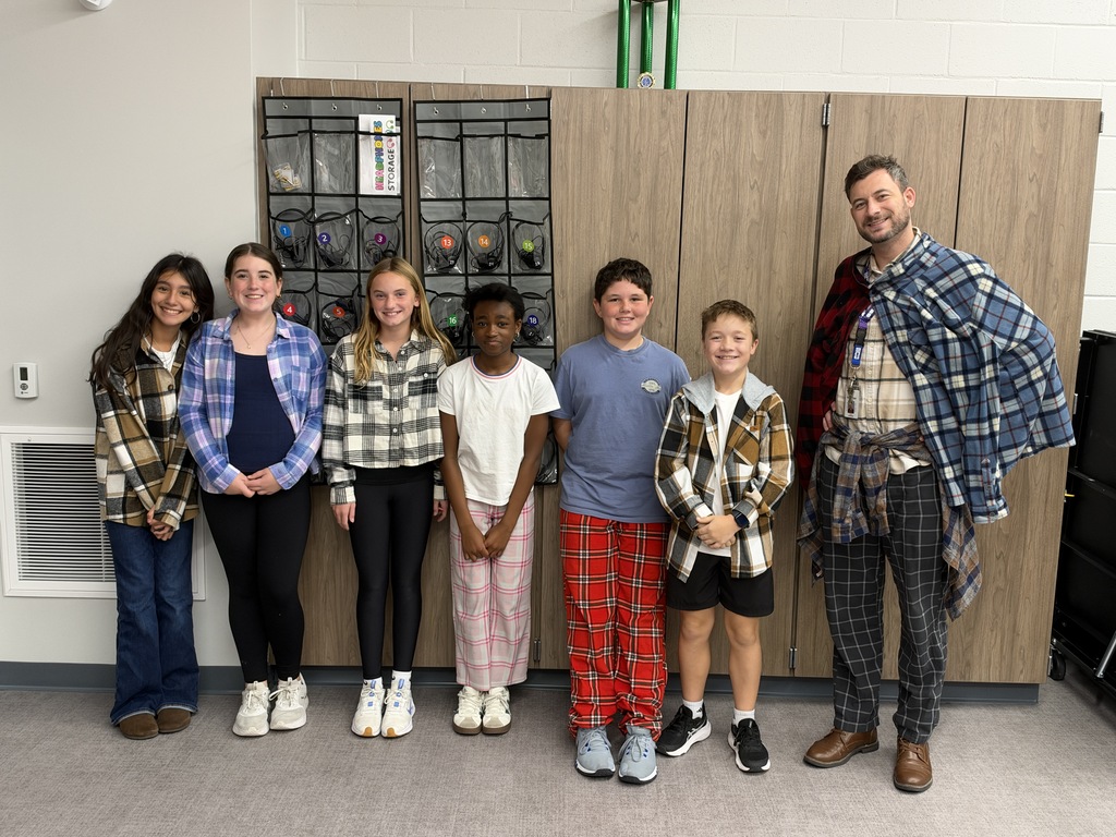Six students and one teacher stand in front of the wall and smile at the camera. They are wearing flannels. 