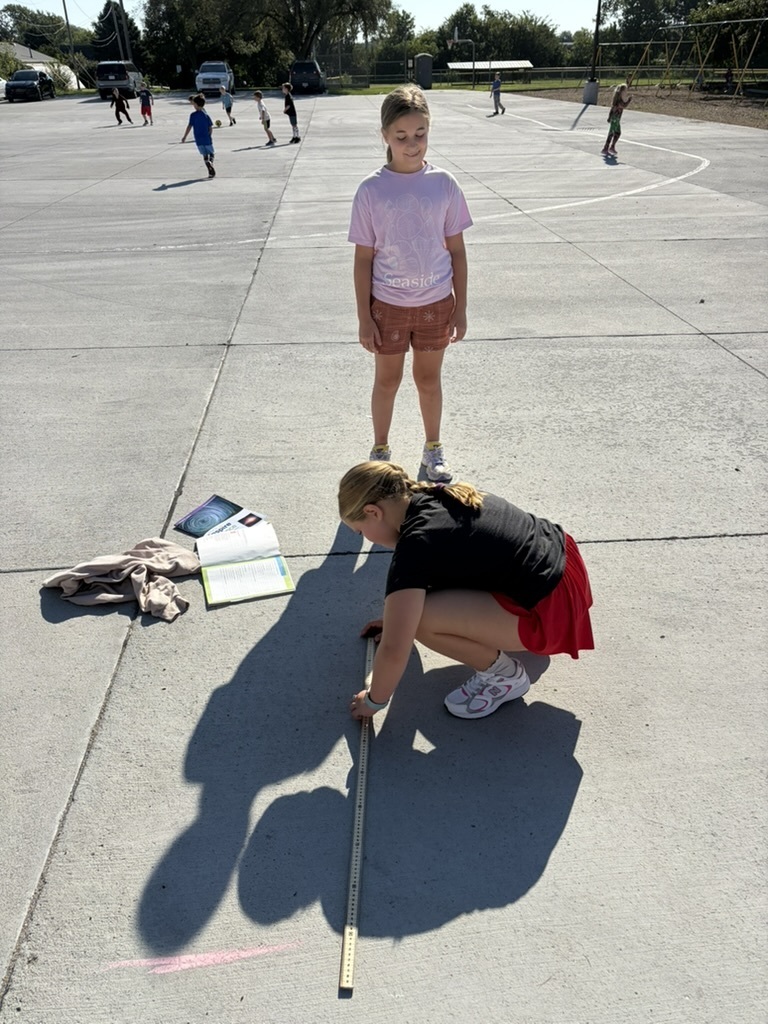 Two students conducting an outdoor science experiment using a meter stick on the school blacktop.