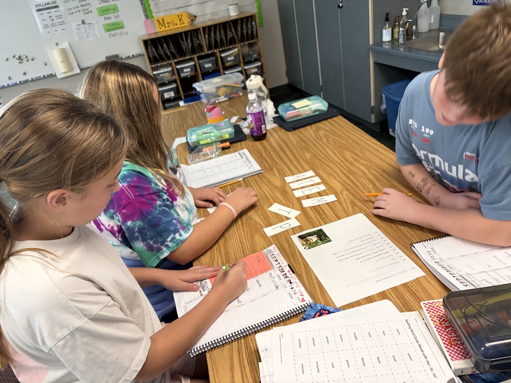 Three students collaborating at a table using letter tiles and word study worksheets.
