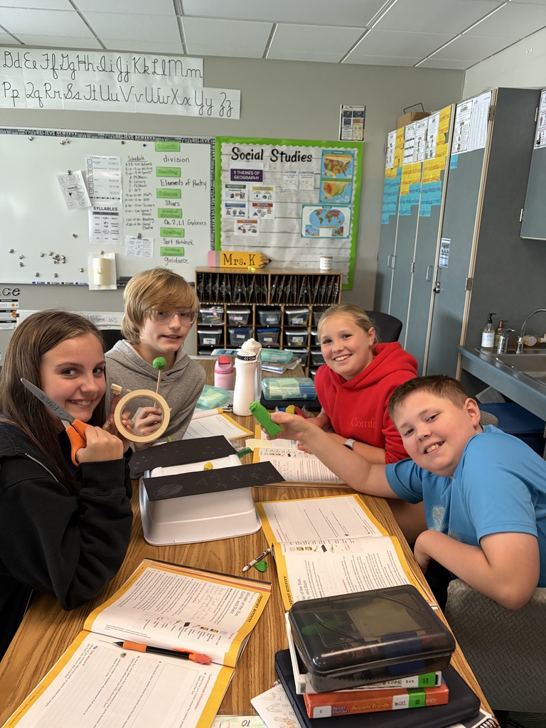 A group of four elementary students smiling around a shared table while working on an interactive science lesson.
