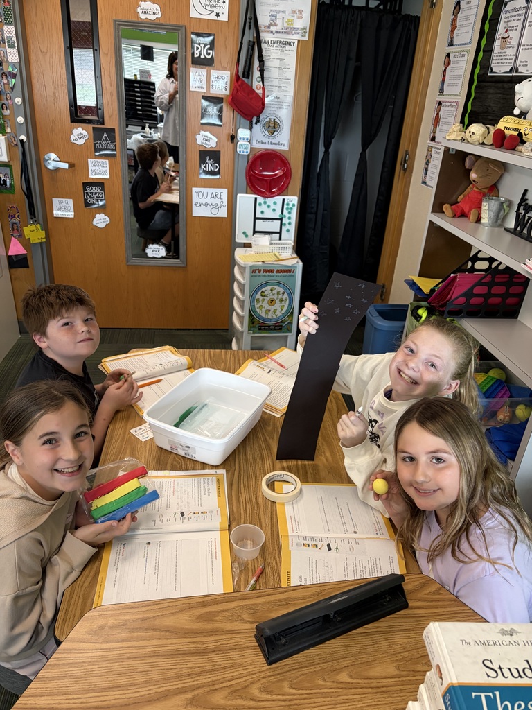 A group of four students smiling at a table while working on a hands-on activity with modeling clay and activity sheets.