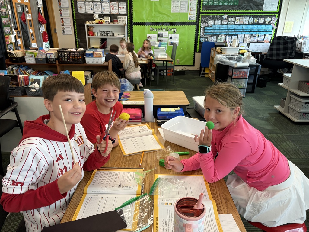 Three students seated at their classroom desks using play dough and wooden skewers during a learning activity.