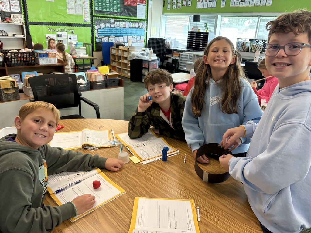 Four students gathered around a wooden table collaborating on a classroom hands-on science project.