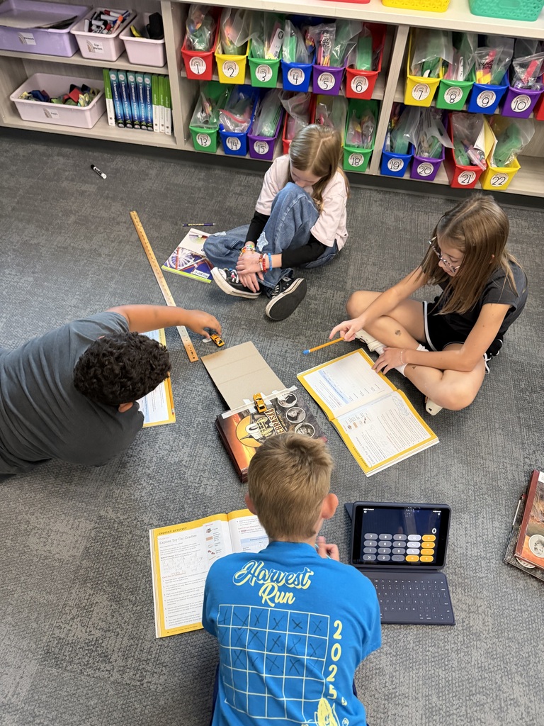students sitting on the ground with a calculator, book, ramp, and yardstick