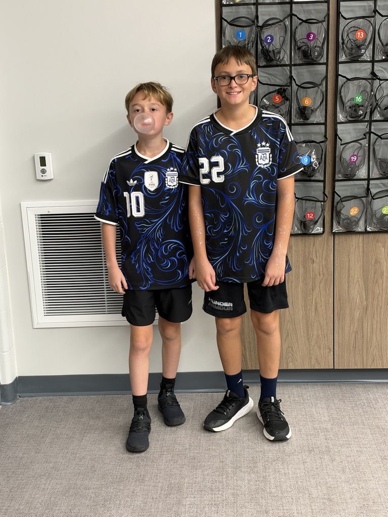 Two boys in matching blue soccer jerseys smile at the camera. 