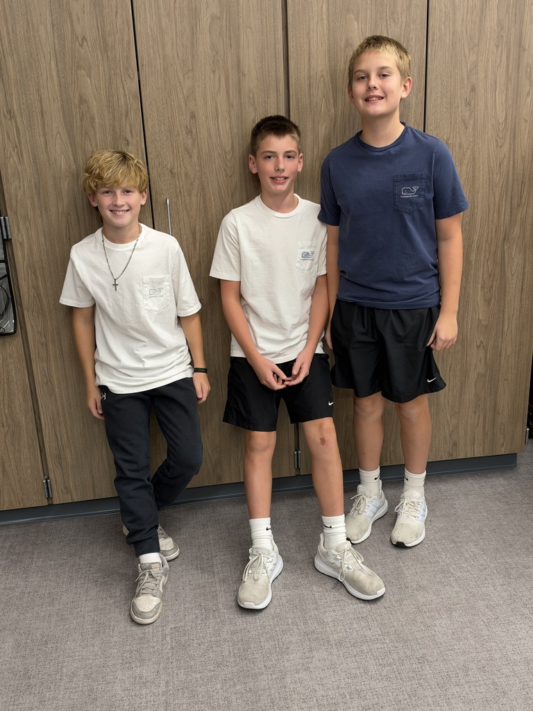 Three boys stand in front of a cabinet and smile at the camera. 