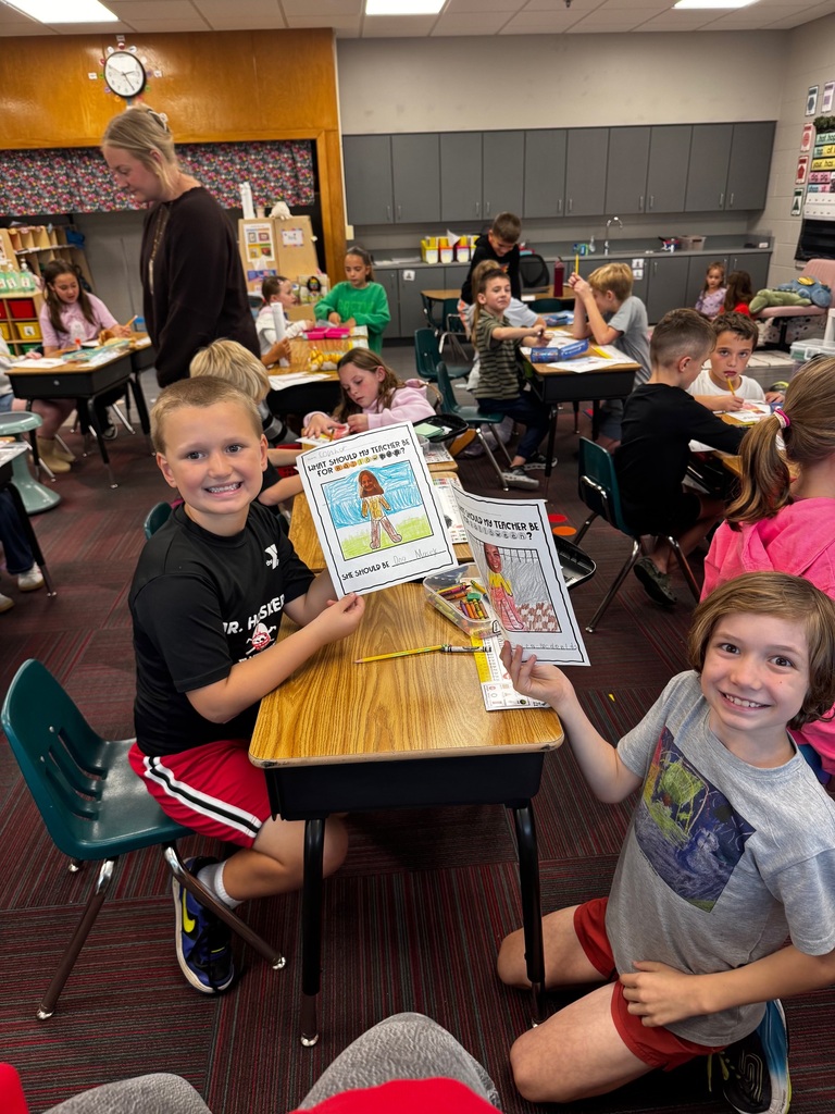 Two boys in a lively classroom setting proudly showing off their colorful Halloween drawing activities.