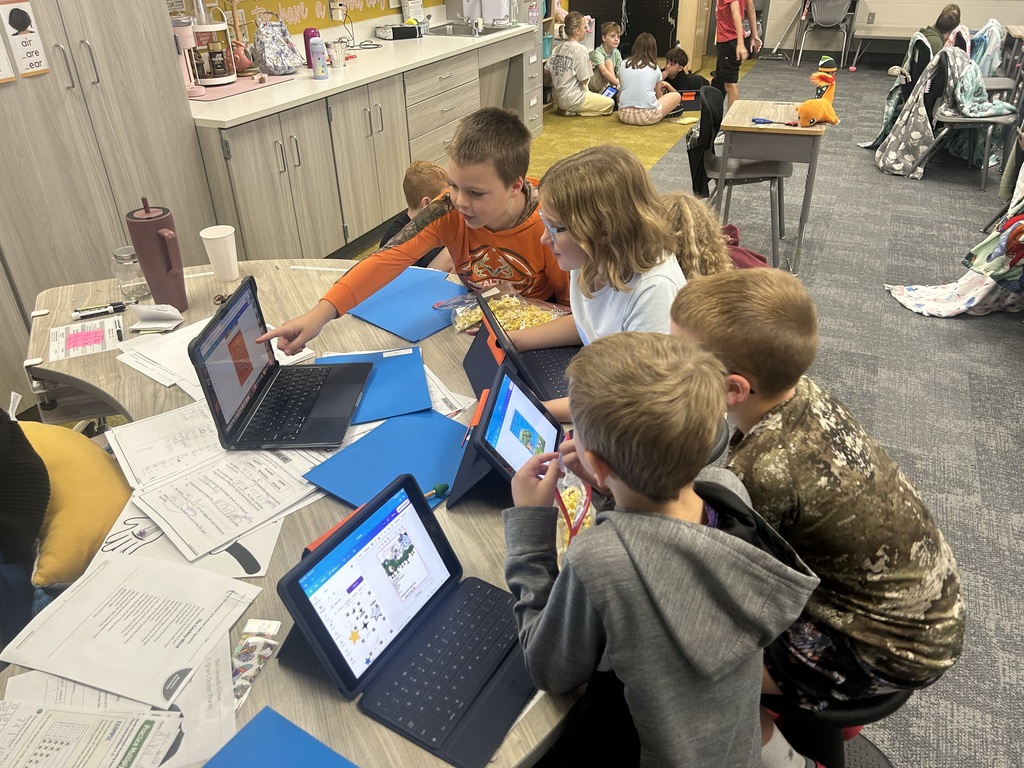 students sitting at a table sharing their movie posters on ipads