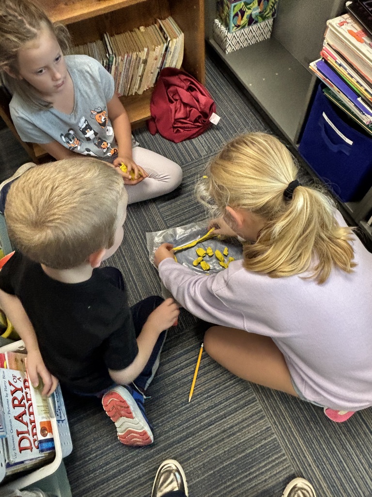 Three students sitting together in a carpeted reading corner shaping yellow play dough on a clear mat.
