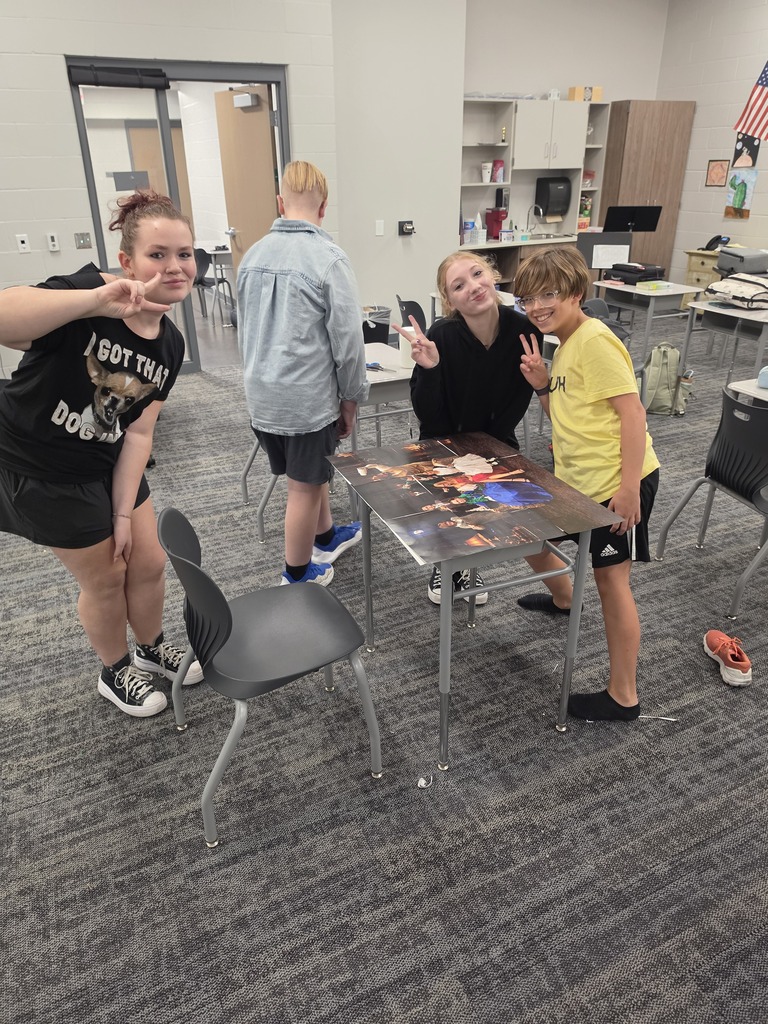 A group of four students are smiling at the camera and giving the peace sign. 